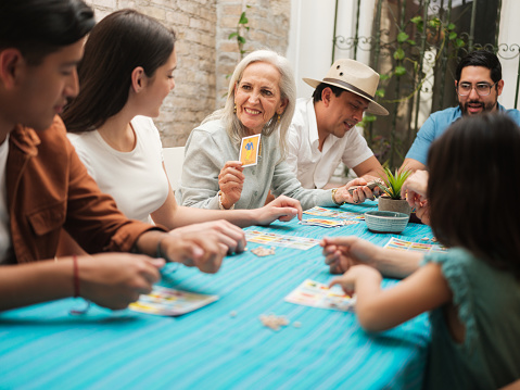 A smiling Mexican grandmother sitting with her family playing a traditional Mexican game of lottery.