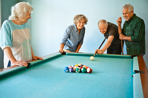 Elderly friends playing pool ball. Senior men and woman are having fun together at nursing home. They are wearing casuals.