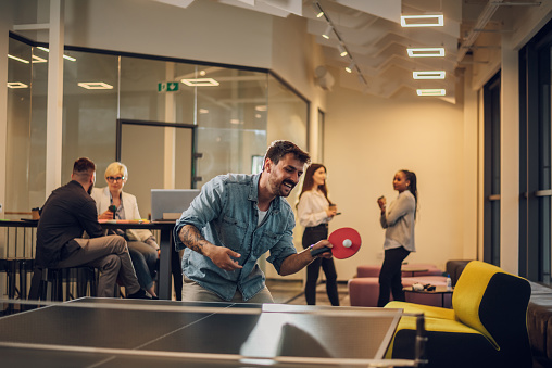 Games between employees during a work break. Colleagues are playing table tennis at work. Having some fun at the office. Portrait of a business man in casual clothes playing ping pong.