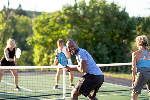 A group of adults have fun while pickleball together on an outdoor court.