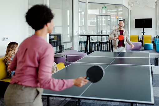 Colleagues playing ping pong table tennis at office break out area. Concept of healthy sport and genuine emotions. Lifestyle, rest concepts