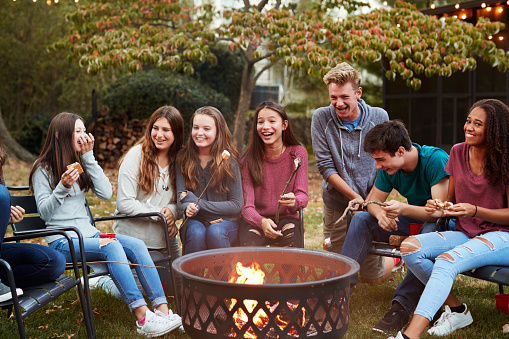 Teenage friends sit round a fire pit toasting marshmallows